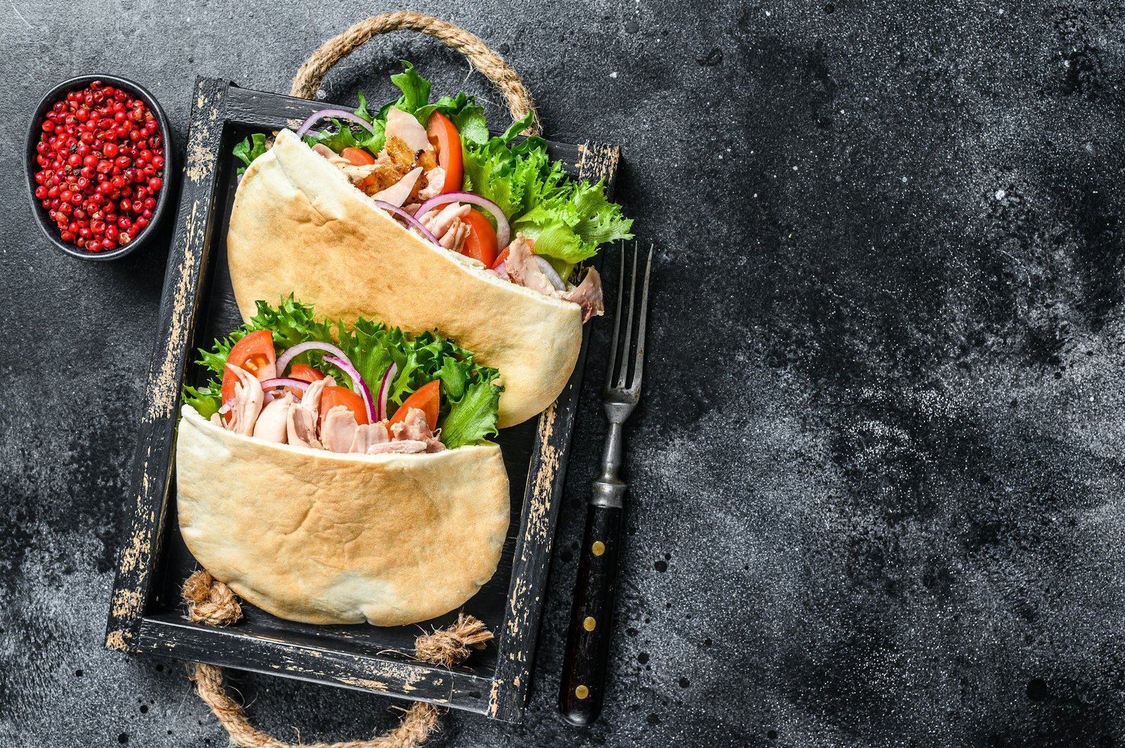 Doner kebab with grilled chicken meat and vegetables in pita bread on a wooden tray.