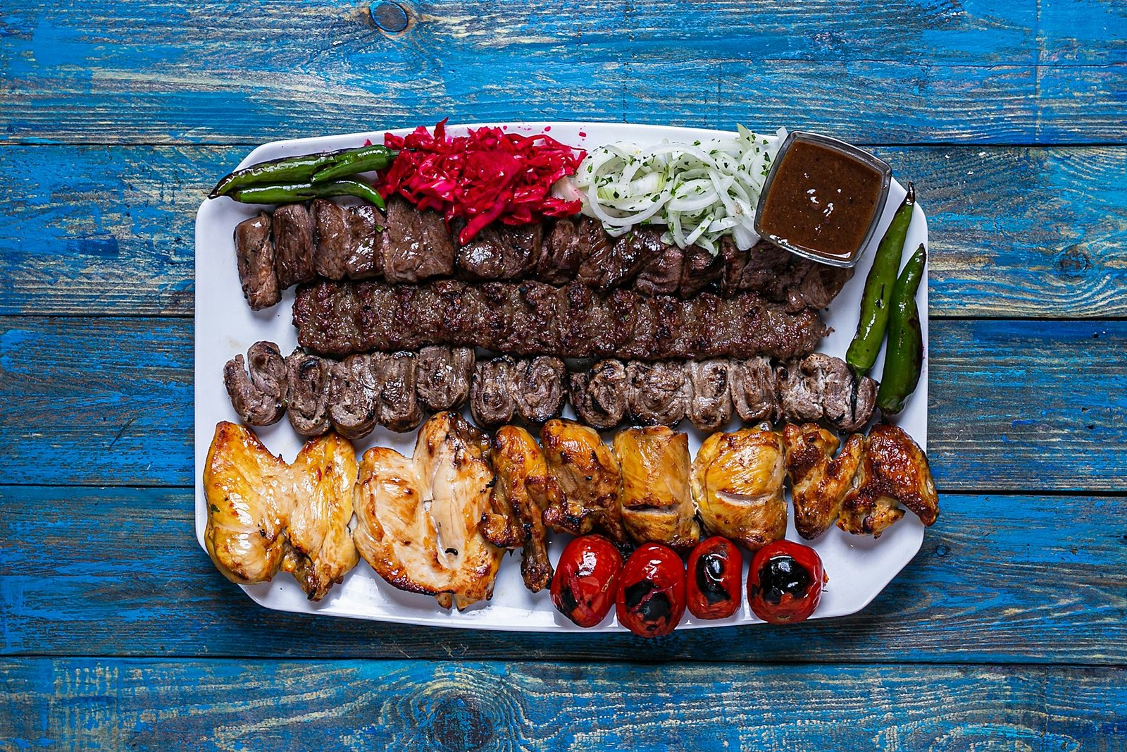 Flat lay mix kebab on a blue wooden table with grilled tomatoes and grilled peppers